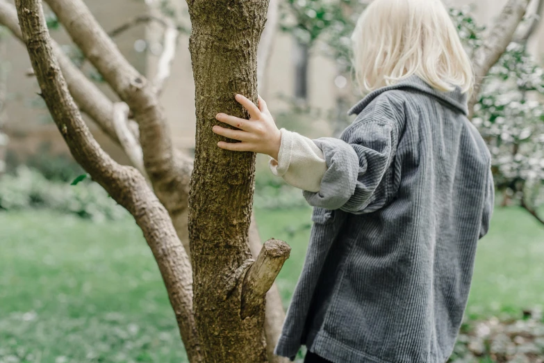 a woman standing next to a tree in a yard, by Emma Andijewska, unsplash, visual art, wearing a jeans jackets, crying and reaching with her arm, wearing hunter coat, spying discretly