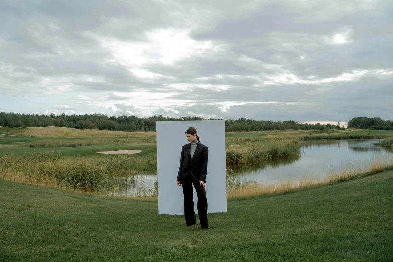 a man in a suit standing in front of a mirror, an album cover, by Attila Meszlenyi, unsplash, surrealism, near pond, outdoor art installation, photo for vogue, uniform off - white sky