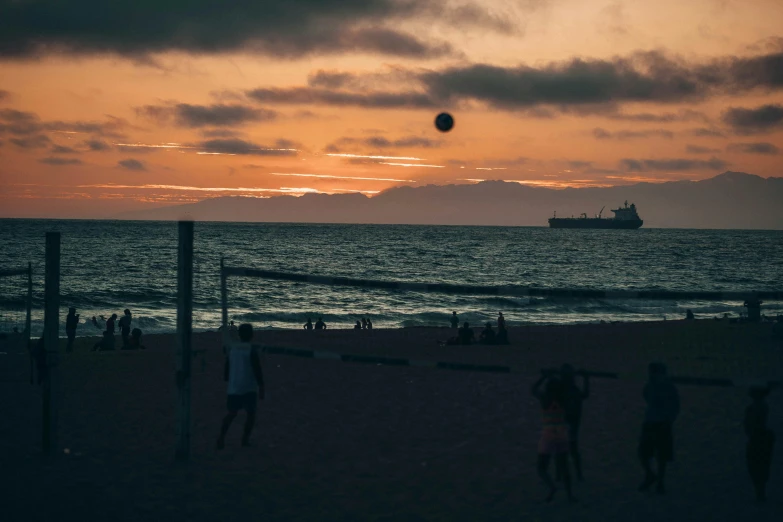 a group of people playing volleyball on a beach, a photo, unsplash contest winner, santa monica beach, sunset in the distance, it's getting dark, profile image