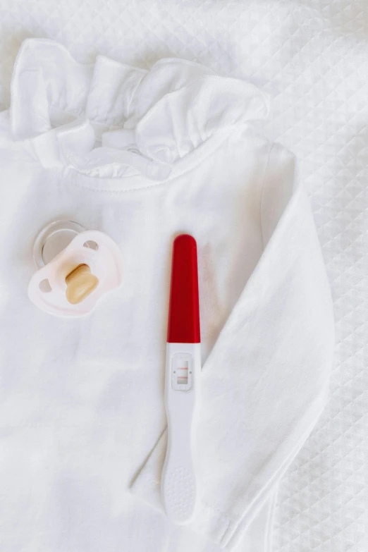 a white shirt sitting on top of a bed next to a baby pacifier, by Nicolette Macnamara, pexels contest winner, dau-al-set, wearing red, lipgloss, formulas, red ballpoint pen