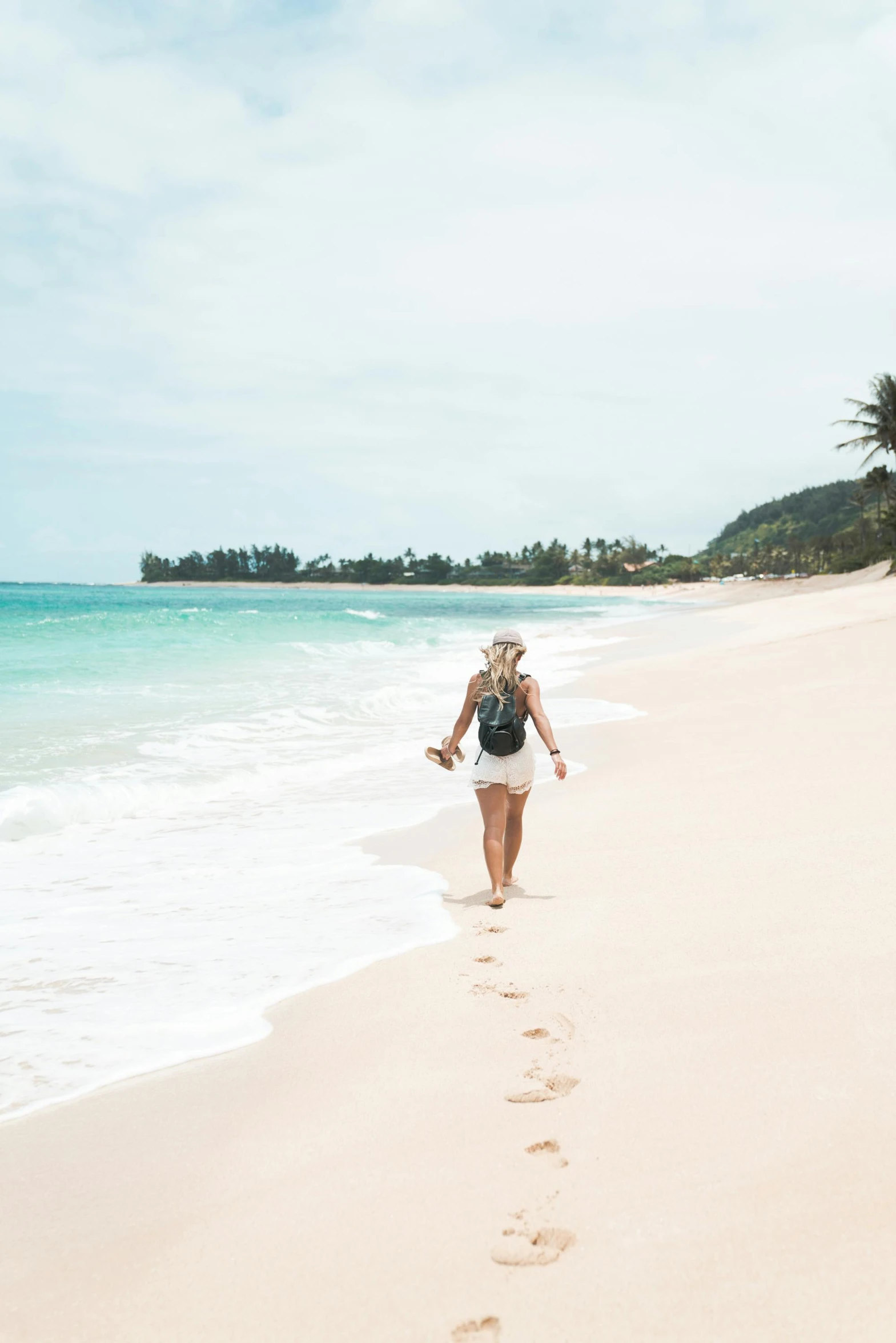 a woman walking on a beach next to the ocean, hawaii beach, beach is between the two valleys, travel guide, slightly tanned