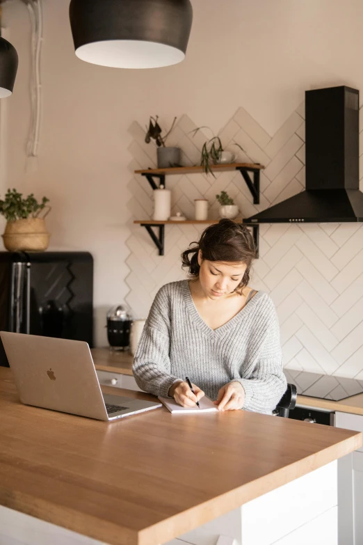 a woman sitting at a kitchen counter working on a laptop, by Nicolette Macnamara, pexels contest winner, small and cosy student bedroom, dwell, writing on a clipboard, profile image