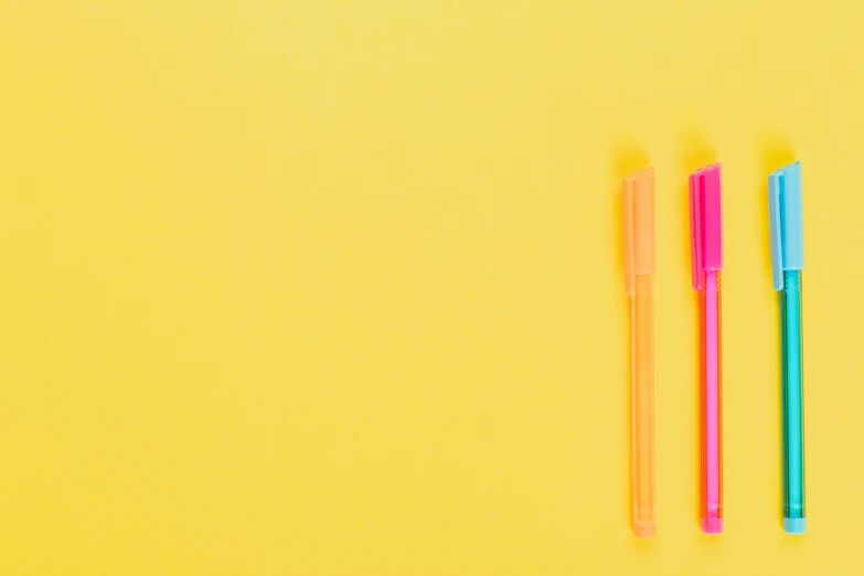 two pens sitting next to each other on a yellow surface, by Nicolette Macnamara, pexels, neon pink, colorful plastic, background image, outline glow