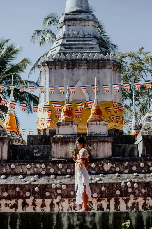 a woman in a white dress standing in front of a building, thai temple, flags, 2019 trending photo, square