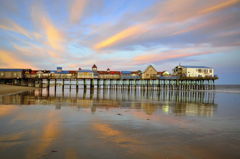 a pier sitting on top of a sandy beach, brightly colored buildings, new hampshire, colorful skies, profile image