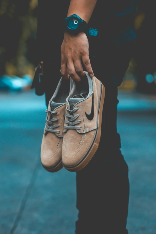 a person holding a pair of shoes in their hand, by Niko Henrichon, pexels contest winner, skateboarder style, muted browns, large)}], thumbnail