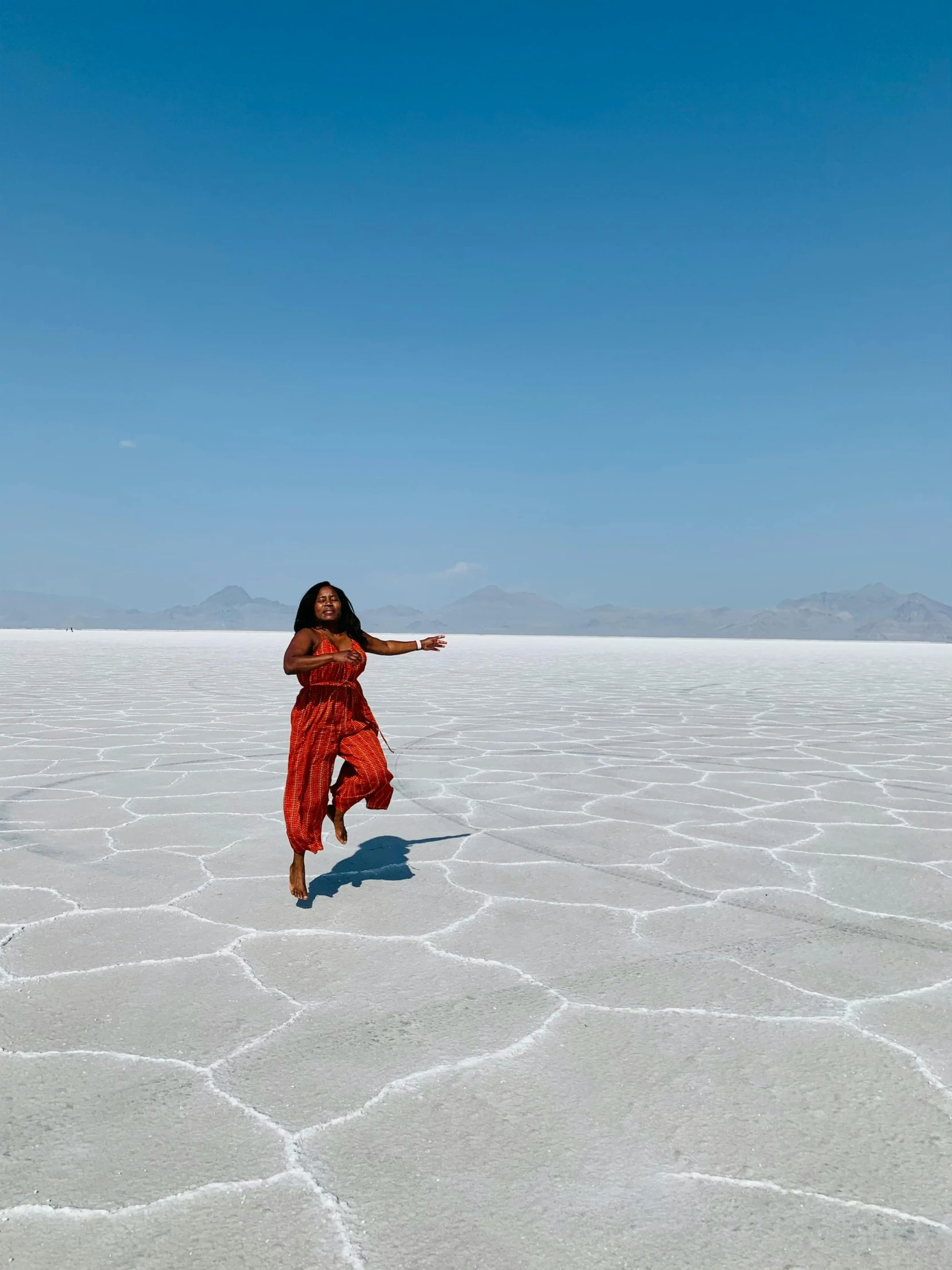 a woman in a red dress is running across the desert, inspired by Scarlett Hooft Graafland, unsplash contest winner, land art, angular dynamic white rock floor, standing in a lake, looking happy, promo image