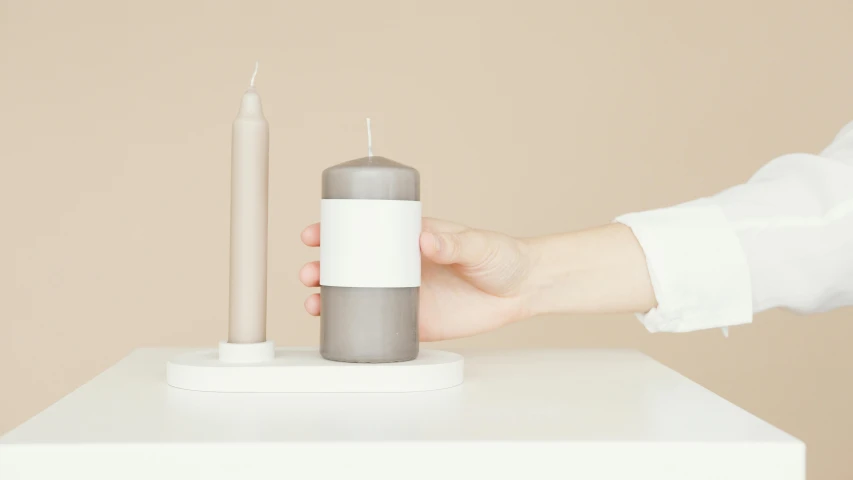 a person holding a candle on top of a table, inspired by Okada Hanko, minimalism, white and grey, muted colours, medium height, presents