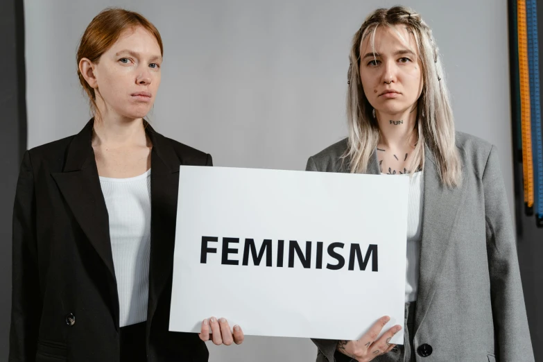 two women standing next to each other holding a sign, trending on pexels, feminist art, background image, profile image, maxim shirkov, close - up studio photo