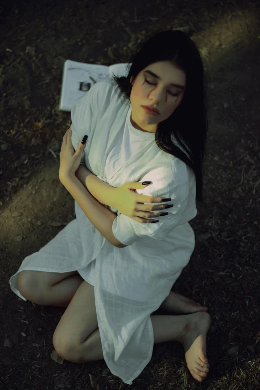 a woman sitting on the ground holding a book, an album cover, inspired by Elsa Bleda, unsplash, art photography, wearing a white hospital gown, crying fashion model, portrait of sadako of the ring, ((portrait))