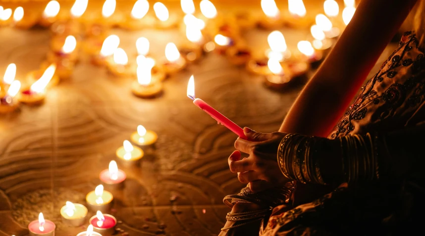 a close up of a person holding a lit candle, lamps on ground, hindu ornaments, profile image, many lights