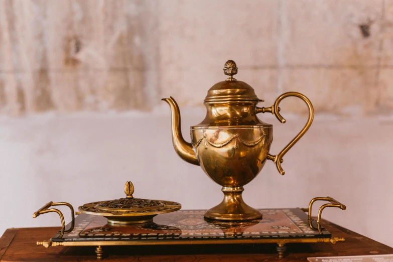 a gold tea pot sitting on top of a wooden table, by Adam Marczyński, pexels contest winner, baroque, french provincial furniture, egyptian style, carrying a tray, thumbnail