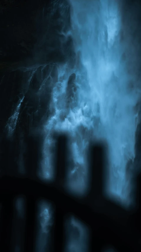 a man standing in front of a waterfall at night, an album cover, by Andrew Geddes, pexels contest winner, hurufiyya, blue smoke, cinematic detail, ghostly figures, blurred