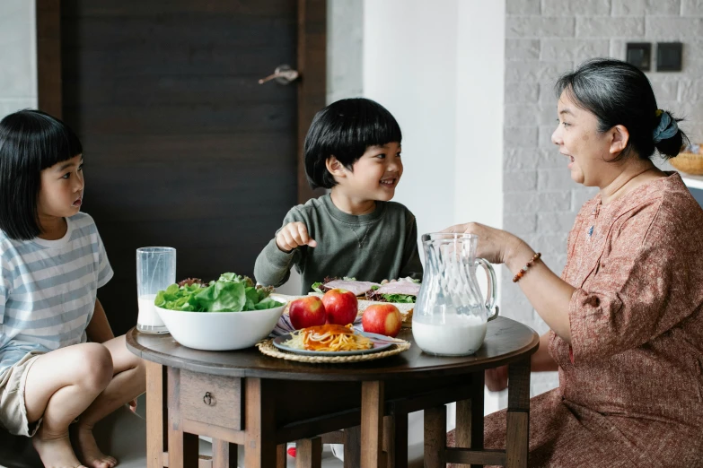 a woman sitting at a table with two children, pexels contest winner, the table is full of food, mutahar laughing, asian male, unique design