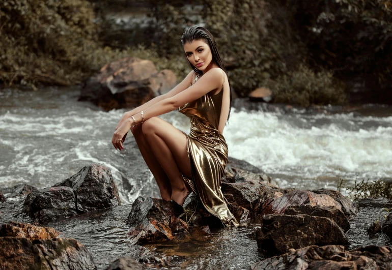 a woman sitting on a rock in a river, by Julia Pishtar, pexels contest winner, elegant gold skin, madison beer, golden dress, portrait of sherlyn chopra