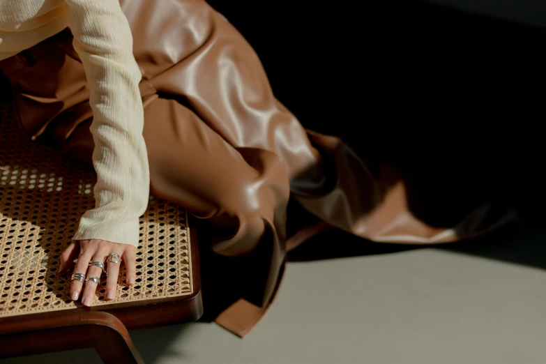 a woman sitting on top of a wooden chair, an album cover, by Emma Andijewska, trending on pexels, leather pouch, long flowing fabric, thumbnail, brown:-2