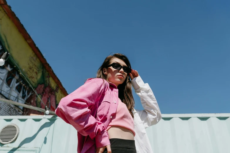 a woman standing in front of a building talking on a cell phone, an album cover, by Lee Loughridge, trending on pexels, visual art, pink shirt, wearing shades, charli bowater, wearing a track suit