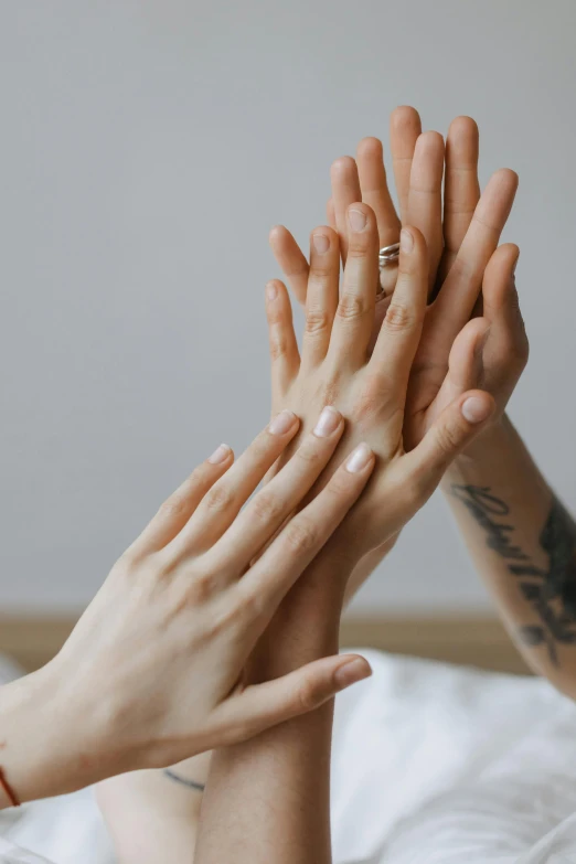 a couple of people laying in bed with their hands in the air, a tattoo, by Matija Jama, trending on pexels, skincare, glowing hands, on a gray background, woman holding another woman