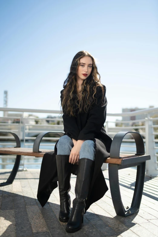 a woman sitting on top of a wooden bench, a portrait, trending on pexels, black coat, young with long hair, promotional image, in the city