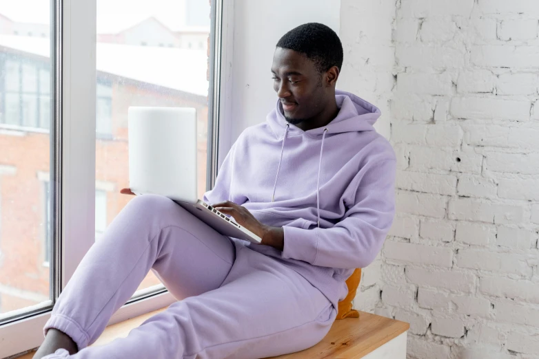 a man sitting on a window sill reading a book, inspired by Frank Mason, trending on pexels, happening, wearing a purple sweatsuit, pastels, jaylen brown, wearing a plug suit