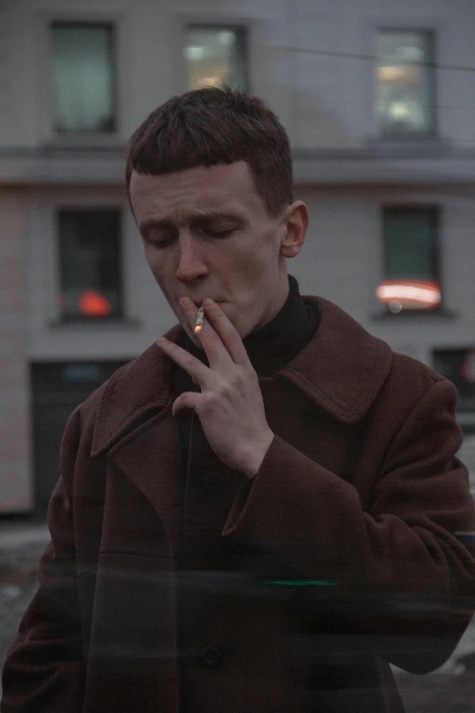 a man smokes a cigarette in front of a building, an album cover, by Attila Meszlenyi, pexels contest winner, wearing a turtleneck and jacket, vitalik buterin, smooth pale skin, cinematic footage