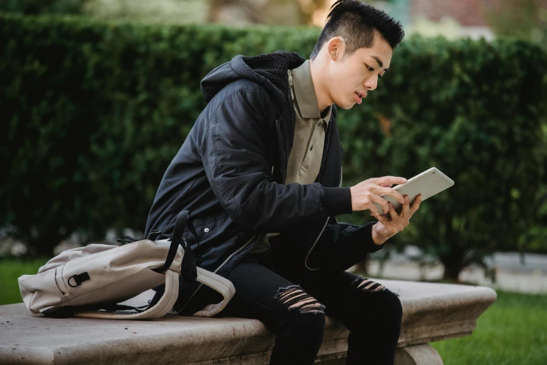 a man sitting on a bench using a tablet computer, a picture, trending on pexels, realism, jin shan and ross tran, wearing jacket, holding books, he is at college