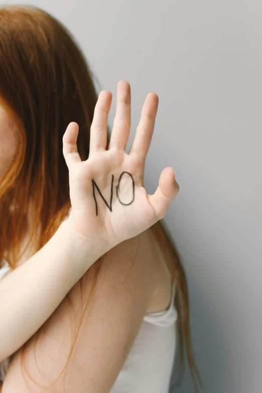 a woman with no written on her hand, by Arabella Rankin, pexels, antipodeans, subject action : holding sign, teenage no, no mustache, a redheaded young woman