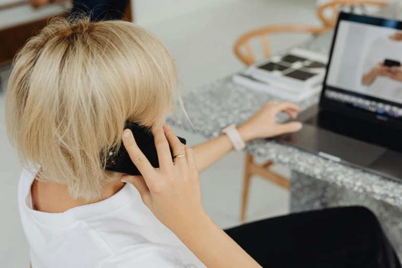 a woman sitting in front of a laptop talking on a cell phone, by Lee Loughridge, trending on pexels, royal commission, from back, local conspirologist, with head phones