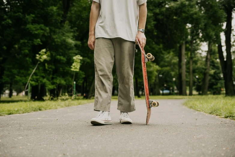 a man standing on a sidewalk holding a skateboard, pexels contest winner, brown pants, in the park, plain background, khakis