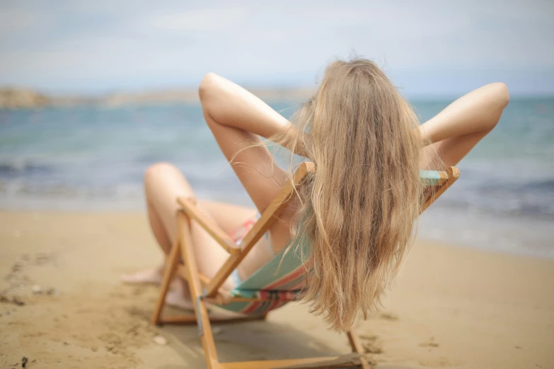 a woman sitting in a chair on a beach, pexels contest winner, renaissance, straight stiff dry damaged hair, deep tan skin, long strawberry - blond hair, sunbathing at the beach