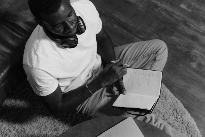 a man sitting on a couch with a book and headphones, a black and white photo, pexels, visual art, pencil drawing of mkbhd, writing in journal, sitting on the floor, handsome hip hop young black man