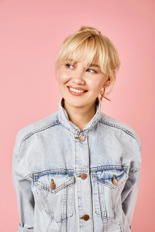 a woman in a denim jacket posing for a picture, an album cover, trending on pexels, with round cheeks, platinum blond, happy fashion model, solid background