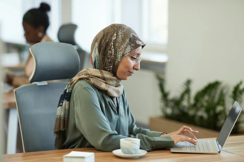 a woman sitting at a table using a laptop computer, inspired by Maryam Hashemi, hurufiyya, medium level shot, thumbnail, in the office, profile image