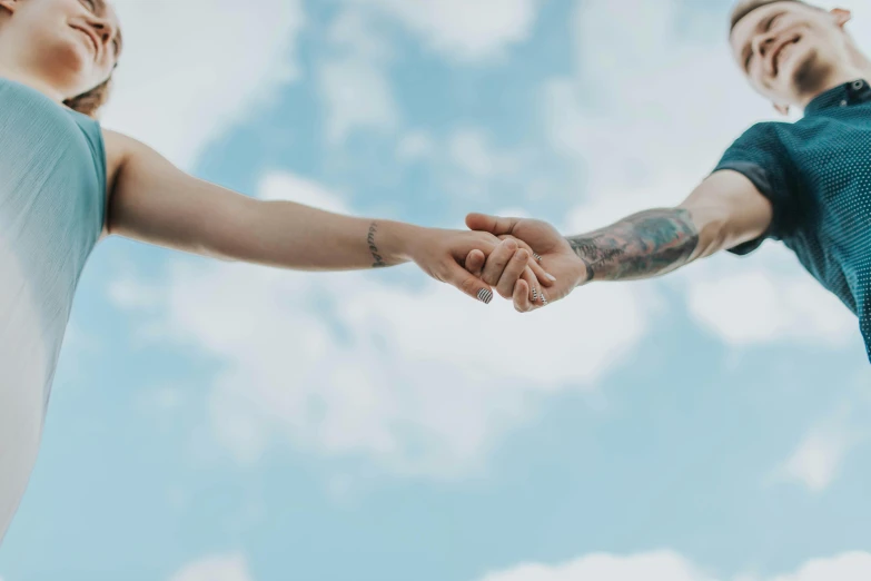 a man and a woman holding hands in front of a blue sky, trending on pexels, cumulus tattoos, background image, connected to heart machines, coloured photo