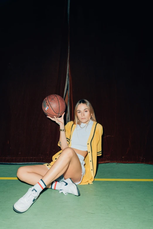 a woman sitting on a basketball court holding a basketball, an album cover, inspired by Elsa Bleda, dribble, sydney sweeney, bra and shorts streetwear, 7 0 s vibe, marie - gabrielle capet style
