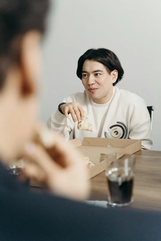 a man sitting at a table with a box of pizza, non binary model, looking at each other mindlessly, inuit, pokimane