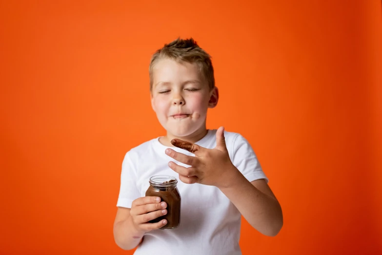 a young boy holding a jar of ice cream, pexels, antipodeans, in front of an orange background, chocolate sauce, manuka, dabbing