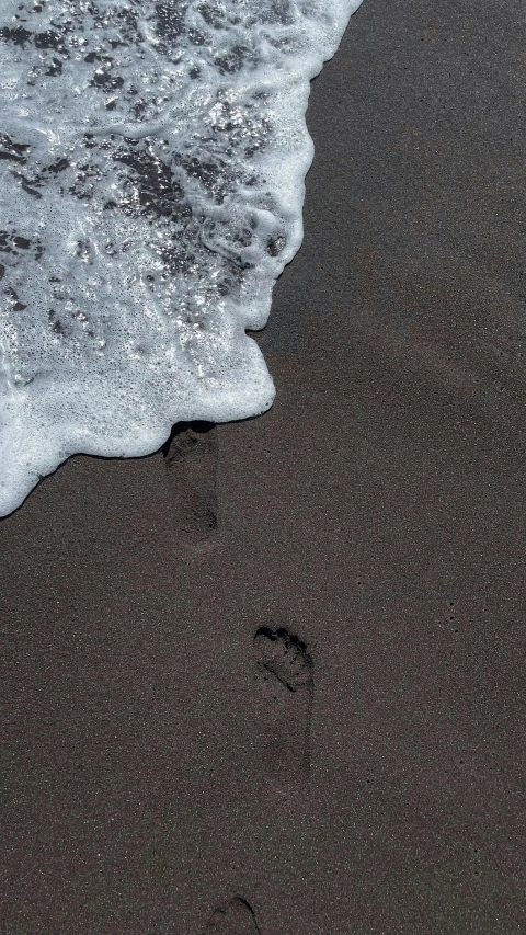 a couple of footprints that are in the sand, by Nina Hamnett, pexels contest winner, ocean wave, black sand, thumbnail, single