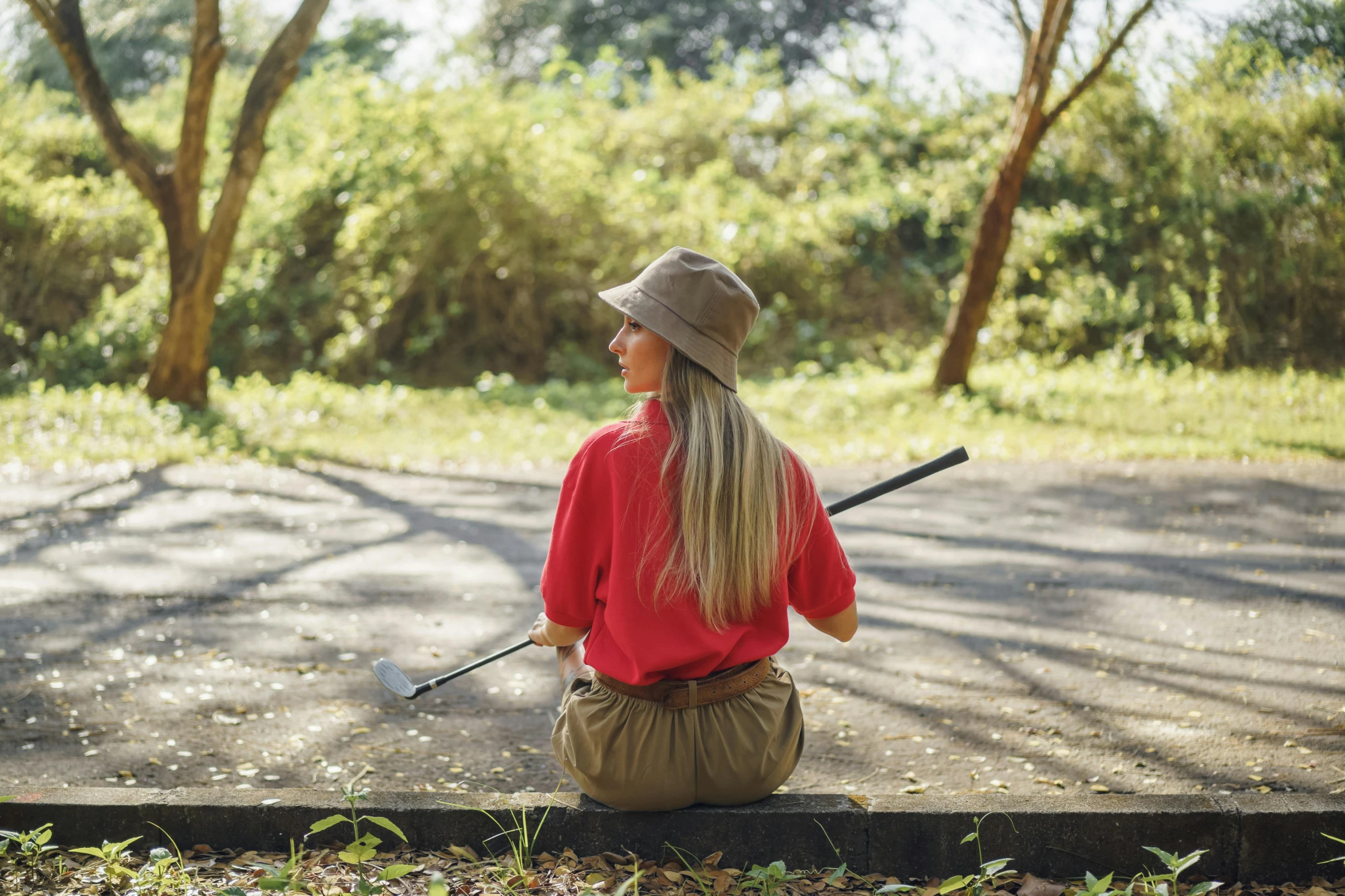 a woman sitting on a curb holding a baseball bat, by Emma Andijewska, pexels contest winner, red shirt brown pants, hiking cane, avatar image, back