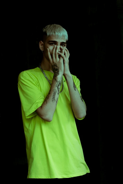 a man in a yellow shirt covers his face with his hands, an album cover, inspired by Elsa Bleda, trending on pexels, antipodeans, bright green hair, justin bieber, ((neon colors)), street clothing