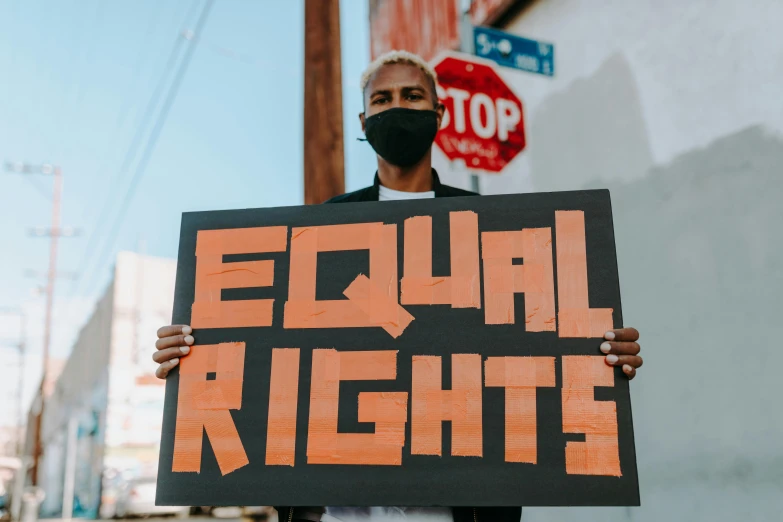 a man holding a sign that says equal rights, an album cover, trending on pexels, diverse, cutout, profile image, brown