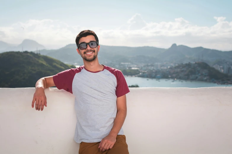 a man standing on top of a white wall, a picture, inspired by Nathan Oliveira, pexels contest winner, happily smiling at the camera, hills in the background, he wears an eyepatch, vacation