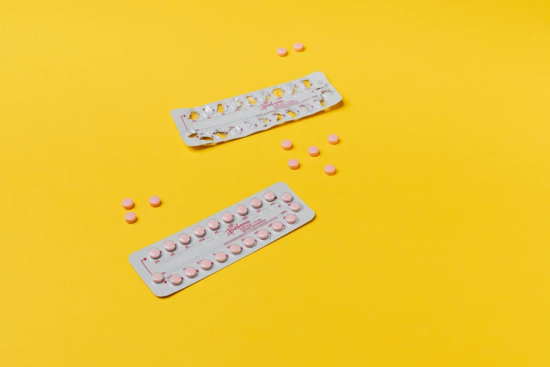 a couple of pills sitting on top of a yellow table, by Ellen Gallagher, trending on pexels, plasticien, pink arches, pair of keycards on table, back facing, on grey background