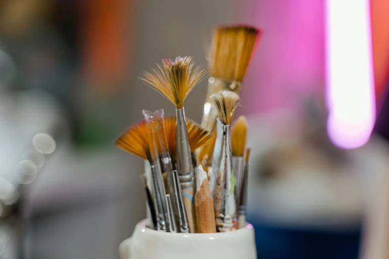 a cup filled with brushes sitting on top of a table, trending on pexels, artstaition, fan favorite, medium close up shot, enamel