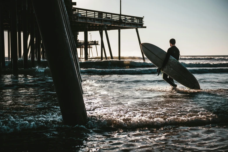 a man carrying a surfboard into the ocean, by Niko Henrichon, unsplash contest winner, renaissance, near a jetty, boardwalk, insanly detailed, late afternoon