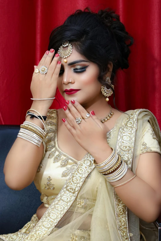 a woman in a sari sitting on a couch, trending on cg society, gold and black makeup, hands on face, rings, 15081959 21121991 01012000 4k