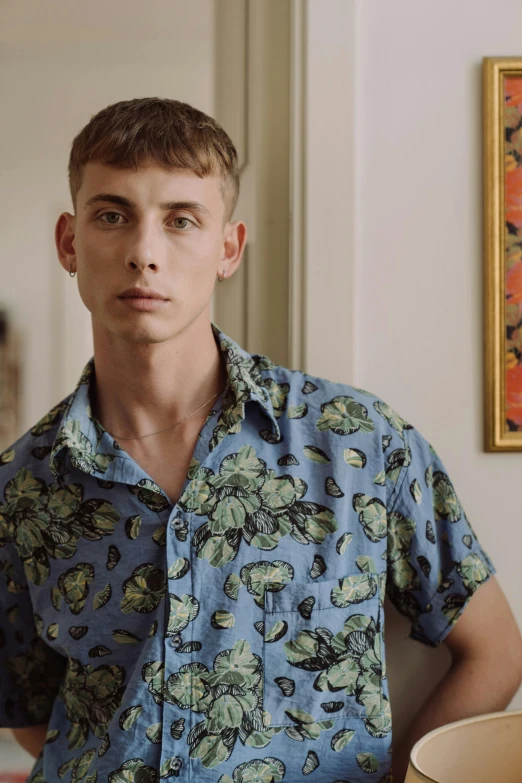 a man sitting at a table with a bowl in front of him, an album cover, by Jessie Alexandra Dick, trending on tumblr, button - up shirt, floral clothes, non binary model, paisley