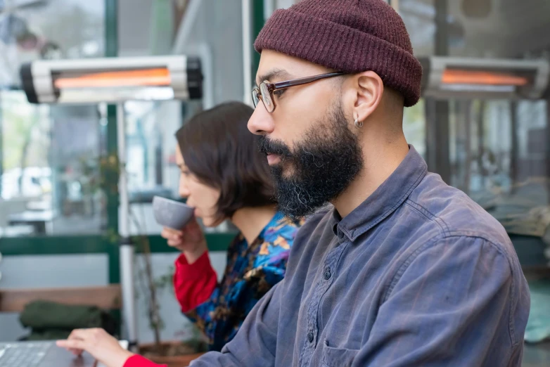 a man sitting in front of a laptop computer, by Edward Avedisian, pexels contest winner, wearing a purple breton cap, 2 people, aboriginal australian hipster, android coffee shop