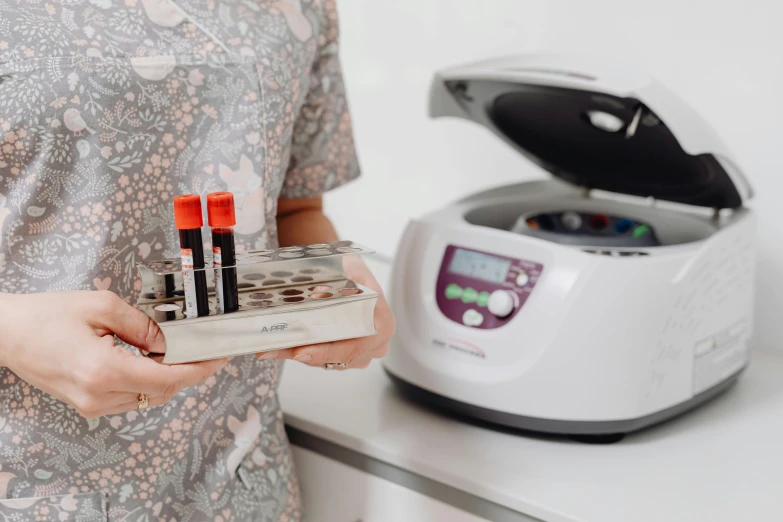 a woman holding a box of lipstick in front of a blender, by Julia Pishtar, private press, pathology sample test tubes, hexadome, trending photo, surgical equipment