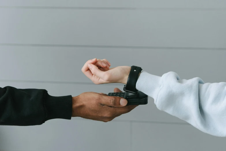 a person handing another person a cell phone, by Carey Morris, trending on pexels, interactive art, leather cuffs around wrists, white and black color palette, healthcare, male and female